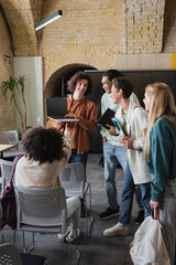 curly man holding laptop with blank screen near cheerful multiethnic classmates.