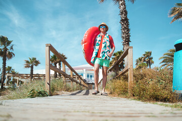 Fototapeta na wymiar young man with inflatable and towel walking on a wooden walkway. Vacation concept.