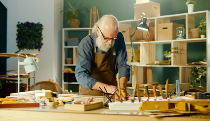 Professional Elderly Man Carpenter Working on Wood Using Carpentry Tools in the Garage. Craft Authentic Workshop. Handicraft, Creative Small Business. Profession, Art and Hobby Concept.