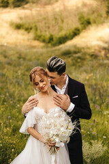 Beautiful newlyweds hugging in nature. Stylish couple together on the background of the hills.