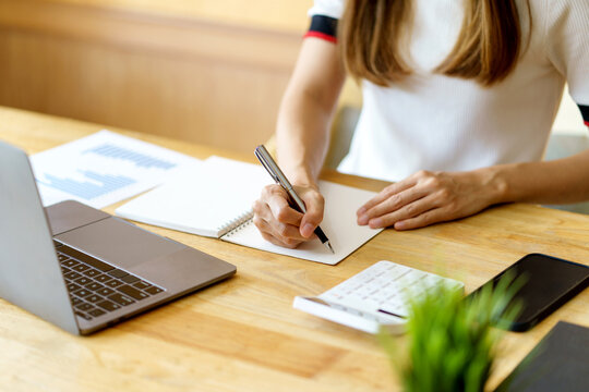 Close up image of a woman writing and taking note on notebook with laptop in office.