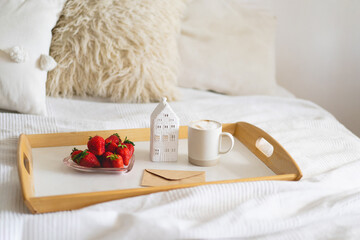 Still life details in home interior of living room. Tray, cup coffee, strawberries and card on a bed. Cozy home
