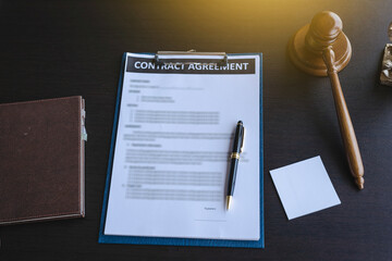 Contract paper on clipboard with lawyer gavel and notebook on black color desk.