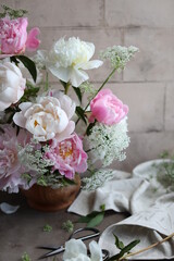 Lush bouquet of white and pink peonies. Floral arrangement of seasonal garden flowers in a wooden bowl. Floral summer still life.