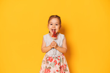 Girl in dress licks watermelon-shaped lollipop against yellow background.