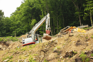Excavator working on construction of higway on the steep slope of the hill.