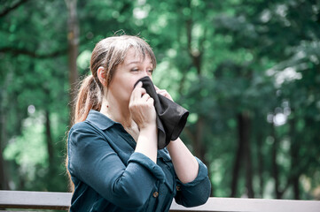 A woman blows her nose into a handkerchief while sitting on a bench in the garden. Spring allergy concept.