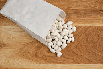 Fototapeta na wymiar heap of white beans in paper bag on wooden background, top view