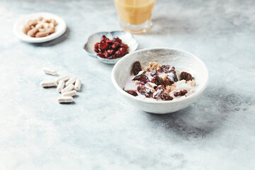 Fototapeta na wymiar Bowl of granola with yogurt, nuts, cranberry and cocoanut. Sport supplements ( carnitine capsules ) in background. Bright stone background. Copy space.