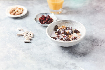 Bowl of granola with yogurt, nuts, cranberry and cocoanut. Sport supplements ( carnitine capsules ) in background. Bright stone background. Copy space.