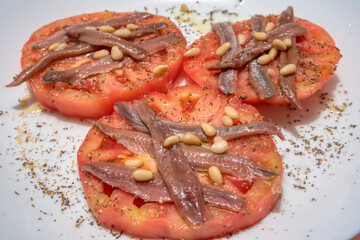 Healthy and tasty food. Three slices of organic tomato with anchovies, pine nuts and spices