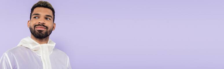 Obraz premium happy and bearded african american man looking away isolated on purple, banner.