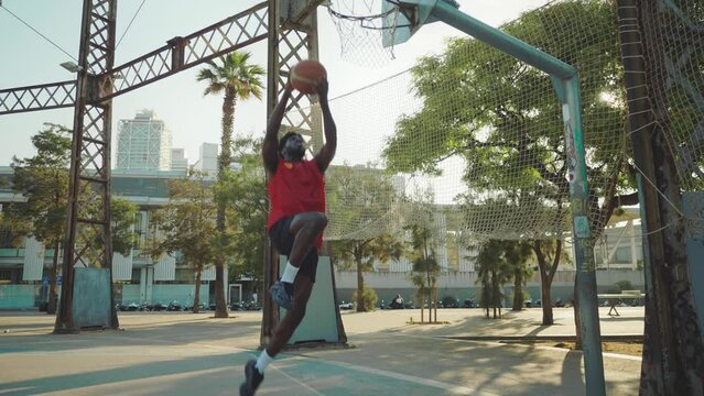 Cinematic footage of a street basketball game outdoor. Basketball players training and having fun at the court doing slam dunks and tricks