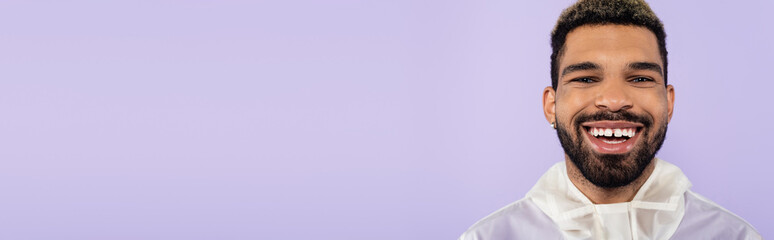Fototapeta premium portrait of happy african american man smiling and looking at camera isolated on purple, banner.