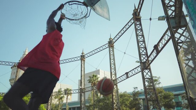 Cinematic footage of a street basketball game outdoor. Basketball players training and having fun at the court doing slam dunks and tricks