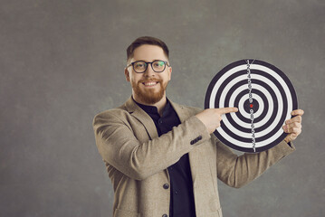 Studio portrait smiling confident young man in suit and hipster glasses looking at camera and pointing finger at shooting target. Concept of setting goals and objectives for achieving business success