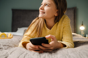 White happy girl using mobile phone while lying on bed