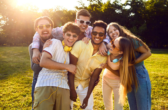 Portrait of happy diverse friends having fun on warm sunny evening in summer park. Bunch of cheerful young people standing on green lawn, smiling and posing for funny group photo together