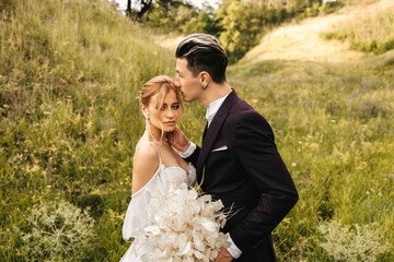 Stylish beautiful newlywed couple in love kissing together in nature
