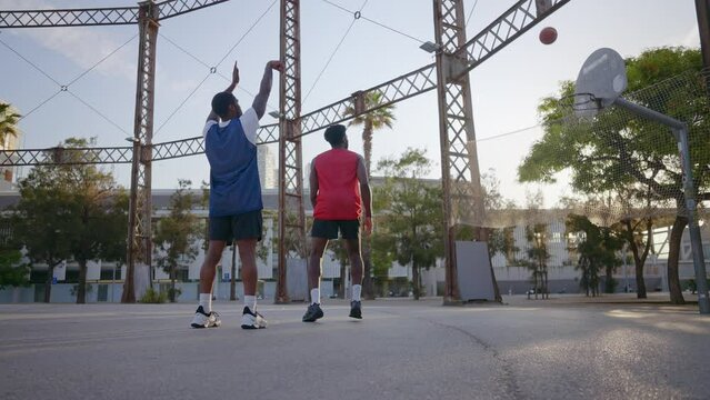 Cinematic footage of a street basketball game outdoor. Basketball players training and having fun at the court doing slam dunks and tricks