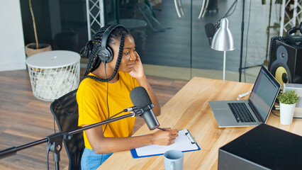 African American Streamer Leads a Podcast and Answers Questions in a Recording Studio, Smiling, Enjoying the Conversation. Podcasts and Audio Blogging Concept.