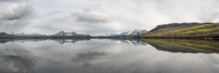 Fototapeta na wymiar Panoramic view of a wilderness lake in Canada during spring with reflection of snow capped mountains in water. 