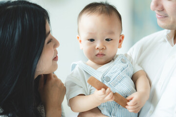 Father's Day concept, young Asian father holding a baby child with family person at home, happy childhood with love and care together, little cute son with dad and parent, parenthood lifestyle