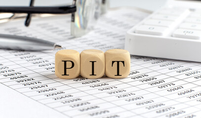 wooden cubes with the word PIT on a financial background with chart, calculator, pen and glasses, business concept.