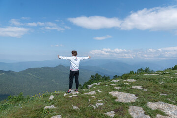Backview of young female standing over top of mountain with hands up and looking on beautiful mountain landscape. Freedom concept