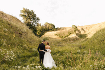 Stylish couple of newlyweds walking hugging on the background of nature