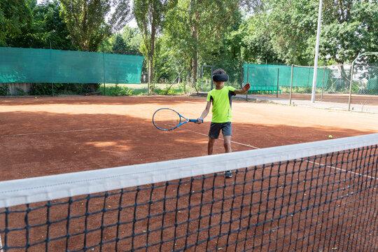 Boy in vr glasses on tennis court behind net with raquet in his hands. Training process in cyberspace with virtual coach.