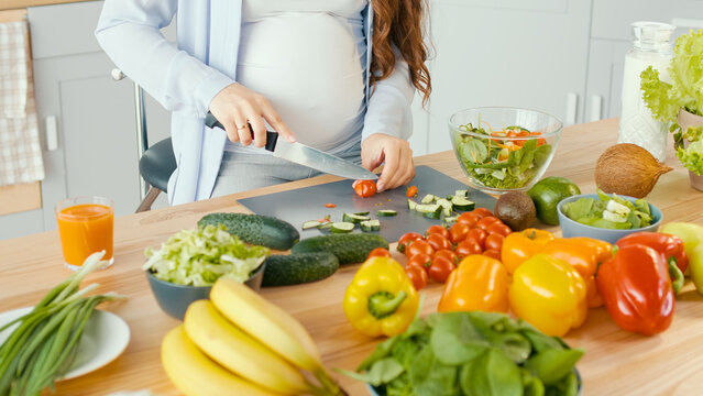 Beautiful Pregnant Woman Happily Preparing a Vegetable Salad, Organic Healthy Food, in a Cozy Home Kitchen. The Concept Of Diet, Proper Nutrition, Healthy Pregnancy and People.