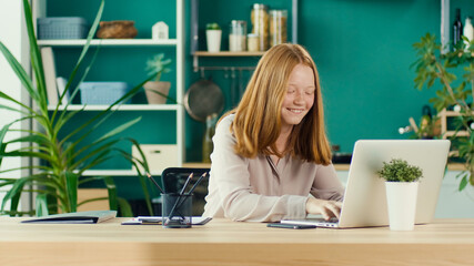 Joyful Red Haired Teenage Girl Studying Online, Comfortable Home Teaching Online in Virtual Classroom Lesson with a Teacher on a Laptop at Home. Education and Homeschooling of Children. Mental Health.