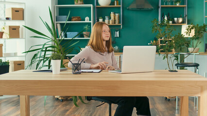 Joyful Red Haired Teenage Girl Studying Online, Comfortable Home Teaching Online in Virtual Classroom Lesson with a Teacher on a Laptop at Home. Education and Homeschooling of Children. Mental Health.