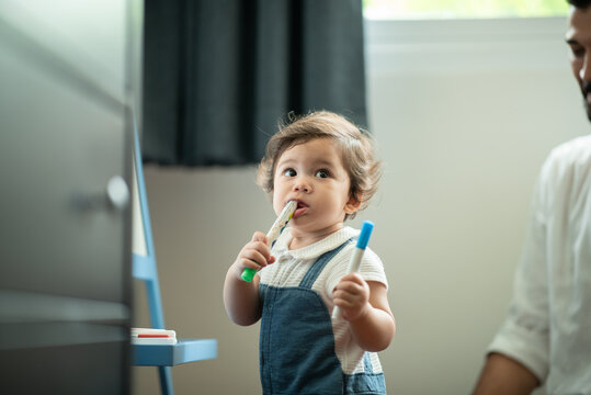 Cute little toddler baby boy playing and chewing marker pen with father while looking away and thinking at home