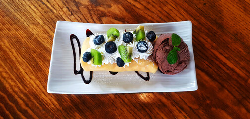 Top view of Chocolate ice cream with sliced fresh kiwi, berry or raspberry and whipped cream in plate or dish on wooden table with copy space at café. Flat lay of Dessert food with freshness fruit.	