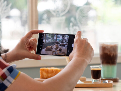 Closeup of women's hands using mobile phone taking photo of dessert and drinks while sitting in comfortable restaurant or coffee shop.