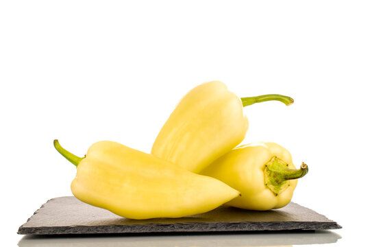 Three bright yellow sweet peppers on a slate stone, close-up, isolated on a white background.