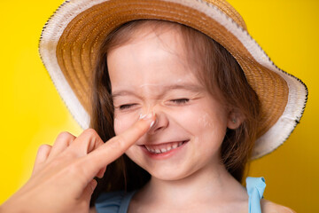 Sun protection. Mom's hand smears toddler daughter with sunscreen. Close-up. Yellow background