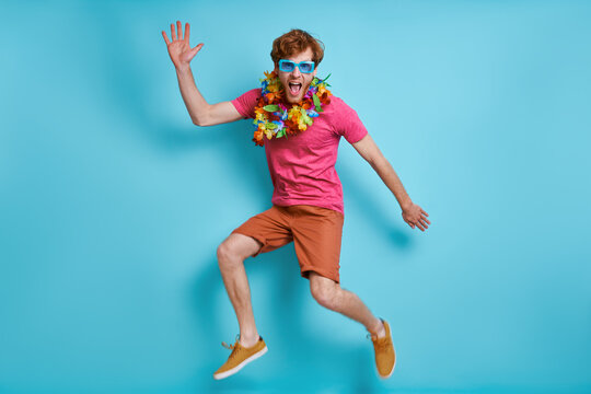 Happy redhead man in Hawaiian necklace jumping against blue background