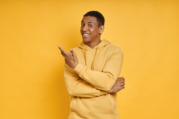 Cheerful mixed race man pointing away while standing against yellow background