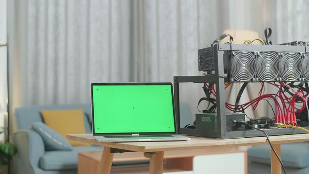 A Green Screen Laptop Is On The Table With Mining Rig For Mining Cryptocurrency 

