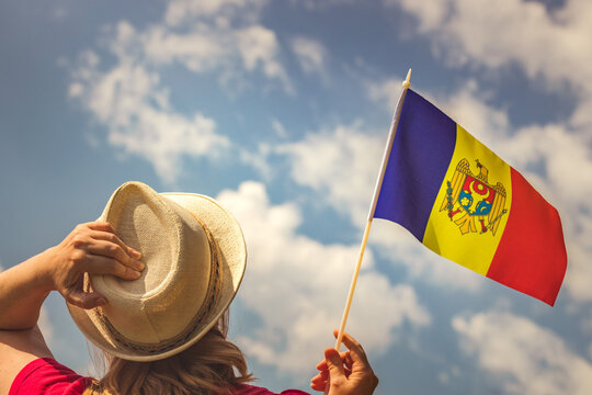 A young woman proudly holds the flag of Moldova above her head while holding up her hat with her other hand, Concept of the holiday of independence and patriotic events