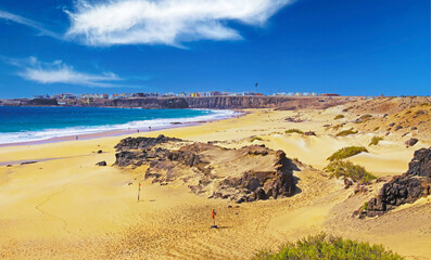 Beautiful sand dunes landscape, empty wild natural beach (Playa del Aljibe), blue atlantic ocean lagoon,  steep cliff with white coastal town (El Cotillo) - North Fuerteventura (focus on lower third)
