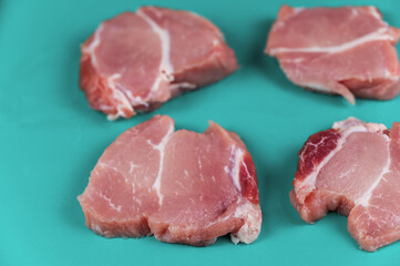 Raw pork opposite turquoise background. Four portioned pieces of pork shoulder ready for further cooking or marinating. Food, ingredients. Selective Focus