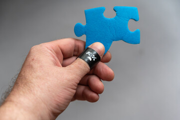 Middle-aged man holds a blue puzzle in his hand. A phalanx of his thumb is wrapped around a black electrical tape. Unhappy face with crossed-out eyes on the ribbon. Failure, negative emotion concept