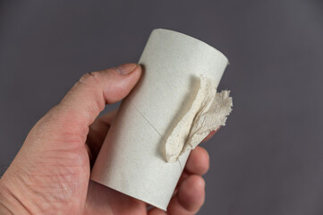 A middle-aged man is holding an empty sleeve of taulet paper. A cylindrical sleeve with a piece of tattered paper in the man's hand. Gray background. Close-up. Selective focus.