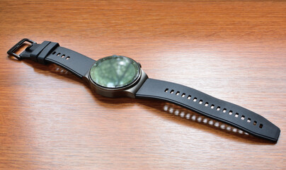 The smartwatch lies on a surface with a wooden texture. Close-up