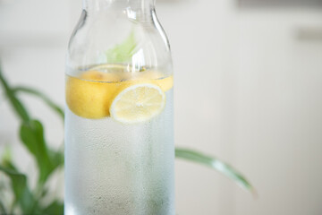 A bottle of water with lemon on pastel light surface. Water with lemon. Summer refreshing drink. Fresh homemade lemonade with lemon slices.