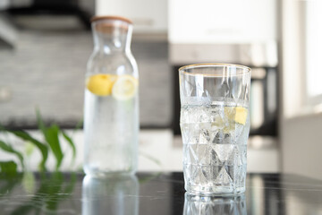 Glass with lemonade in the kitchen. Ice water. Drops of water on a bottle of lemonade. Cocktail with ice and lemon slices.